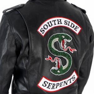 May include: A black leather jacket featuring a large embroidered patch on the back. The patch displays a green snake coiled into an S-shape with red tongues and white fangs, flanked by white banners with red borders reading SOUTH SIDE and SERPENTS.