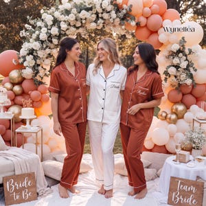 Può includere: Tre set di pigiama coordinati composti da camicie a maniche corte con bottoni e pantaloni lunghi. Due set sono di colore ruggine, mentre il set centrale è bianco. Ogni camicia presenta profili a contrasto e testo ricamato sul taschino.