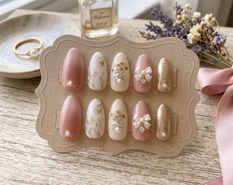 Uñas postizas elegantes en rosa empolvado con diseño floral dorado / Uñas románticas de novia con lazo blanco 3D y perla / Uñas de boda con brillo almendrado