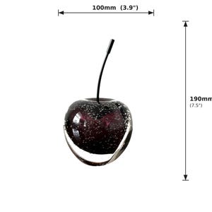 May include: A decorative glass cherry sculpture. The cherry is a deep purple color with air bubbles and a clear glass exterior. It measures 7.5 inches tall and 3.9 inches wide.