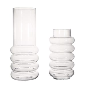 May include: Two clear glass vases. The taller vase is cylindrical with a rounded base and four stacked, bubble-like rings. The shorter vase has a similar design, with a rounded base and three bubble-like rings. Both vases are empty and sit on a white background.