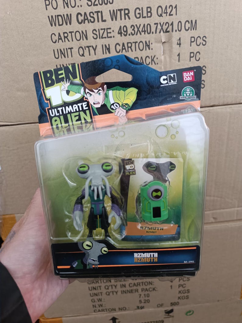Puede incluir: Una figura de acci&oacute;n de Azmuth de Ben 10 Ultimate Alien en un paquete de pl&aacute;stico transparente. La figura es gris, morada y negra. El paquete tambi&eacute;n incluye un dispositivo verde. El embalaje presenta el logotipo de Ben 10 y un personaje de dibujos animados.