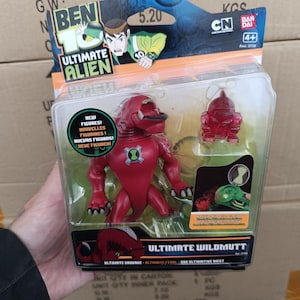 以下が含まれることがあります： ベン10アルティメットエイリアンのアクションフィギュアセット。パッケージには、赤いワイルドマットのフィギュアと、より小さな半透明の赤いフィギュアが描かれています。パッケージには「NEW FIGURES！」と「ULTIMATE WILDMUTT」の文字が含まれています。パッケージには、Cartoon NetworkとBandaiのロゴも表示されています。