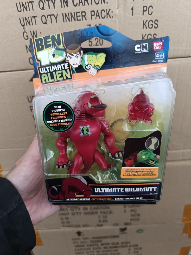 以下が含まれることがあります： ベン10アルティメットエイリアンのアクションフィギュアセット。パッケージには、赤いワイルドマットのフィギュアと、より小さな半透明の赤いフィギュアが描かれています。パッケージには「NEW FIGURES！」と「ULTIMATE WILDMUTT」の文字が含まれています。パッケージには、Cartoon NetworkとBandaiのロゴも表示されています。