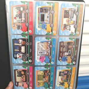 May include: A black card binder holding nine colorful trading cards. Each card features a unique character and interior scene, with names like Vivian, Hopkins, and June. The cards are in a protective sleeve.