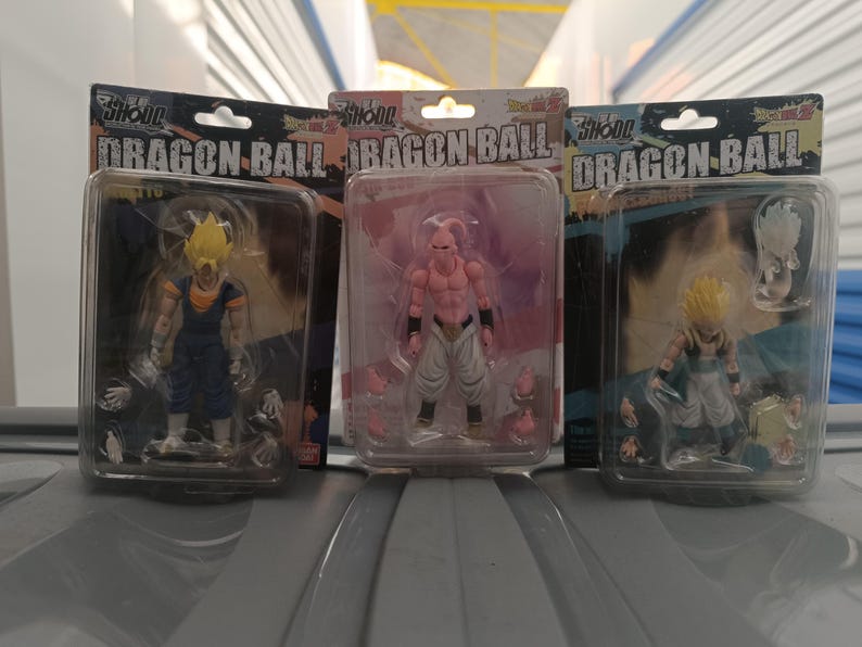 Puede incluir: Tres figuras de acci&oacute;n de Dragon Ball en embalajes de pl&aacute;stico transparente. Las figuras son de varios personajes con dise&ntilde;os detallados y colores vibrantes. El embalaje incluye el texto "Dragon Ball" y los nombres de los personajes.