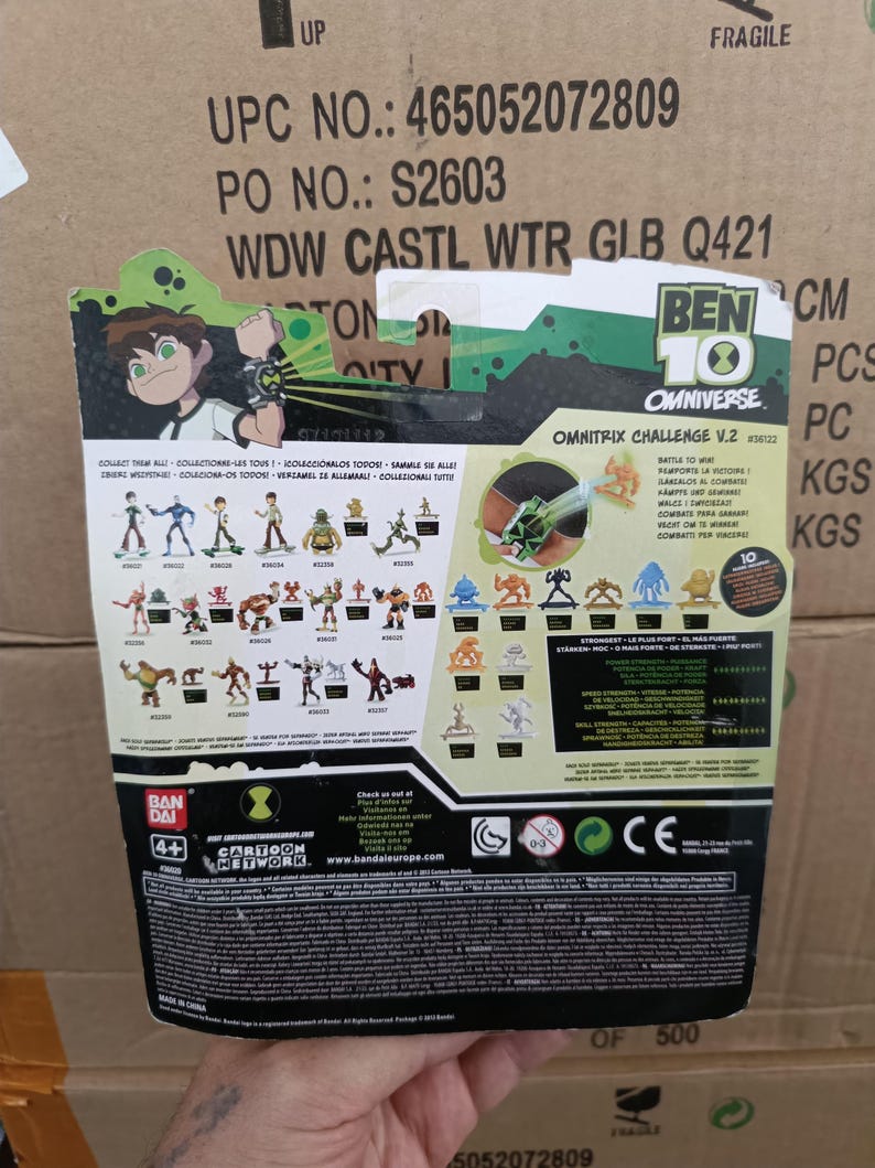 May include: The back of a Ben 10 Omnitrix Challenge V.2 toy package. The package features cartoon illustrations of characters and the Ben 10 logo. The package includes the text "Collect Them All" and "Battle to Win".