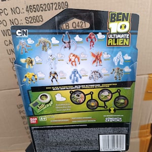 Op de afbeelding: Achterkant van een Ben 10 Ultimate Alien speelgoedverpakking. De verpakking bevat verschillende illustraties van buitenaardse personages en het Cartoon Network-logo. De tekst "DISC BLIEN ULTIMATRIN" en "4+" is inbegrepen.