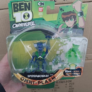 May include: A Ben 10 Omniverse SpiderMonkey Omni-Plasm action figure in a clear plastic package. The figure is blue and green, with a detailed design. The packaging includes the Ben 10 logo, CN, and Bandai branding. The package dimensions are 40.7 x 21.0 cm.