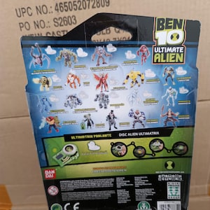 Op de afbeelding: Achterkant van een Ben 10 Ultimate Alien speelgoedverpakking. De verpakking bevat illustraties van verschillende alien-personages, het Ben 10-logo en tekst, waaronder "Ultimatrix Parlante" en "Disc Alien Ultimatrix". De achtergrond is blauw en groen.