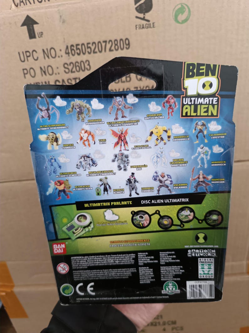 Op de afbeelding: Achterkant van een Ben 10 Ultimate Alien speelgoedverpakking. De verpakking bevat illustraties van verschillende alien-personages, het Ben 10-logo en tekst, waaronder "Ultimatrix Parlante" en "Disc Alien Ultimatrix". De achtergrond is blauw en groen.