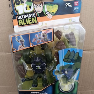May include: A Ben 10 Ultimate Alien action figure of Ultimate Humungousaur in a clear plastic package. The figure is dark green with black and blue accents. The packaging features cartoon graphics and the CN and Bandai logos.