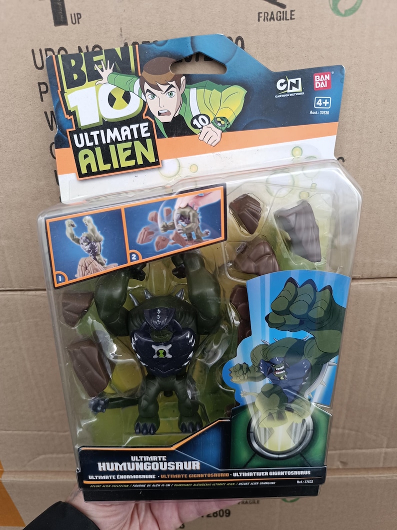 May include: A Ben 10 Ultimate Alien action figure of Ultimate Humungousaur in a clear plastic package. The figure is dark green with black and blue accents. The packaging features cartoon graphics and the CN and Bandai logos.