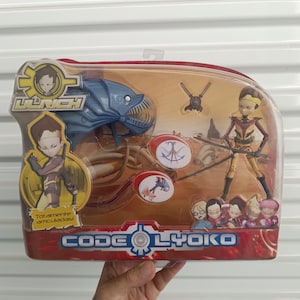 Puede incluir: Un set de figuras de acción de Código Lyoko en un embalaje de plástico transparente. El set incluye múltiples figuras, un monstruo azul y accesorios. El embalaje presenta el texto "LAUNCH" y "CODE LYOKO".