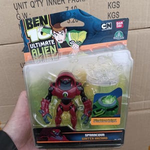 May include: A Ben 10 Ultimate Alien Sparrccour Water Hazard action figure in a clear plastic package. The figure is primarily red and black with a green emblem. The packaging features the Ben 10 logo and Cartoon Network branding.