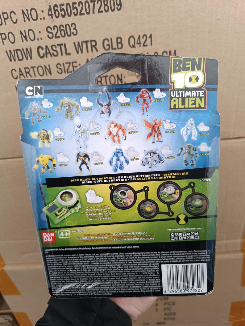 May include: The back of a Ben 10 Ultimate Alien toy package. The package features various alien figures, the Cartoon Network logo, and the text "DISC BLIEN ULTIMETRIE - DE BLIEN ULTIMATRIN - DISKMATRIN". The package also includes the Bandai logo.