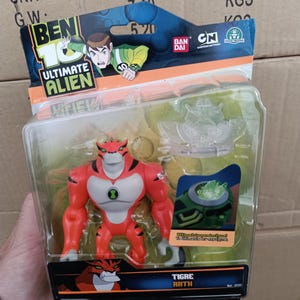 May include: A Ben 10 Ultimate Alien action figure of Tigre Rath, a red and white tiger-like alien, in a clear plastic package. The packaging features the Ben 10 logo, character art, and the text "Tigre Rath".