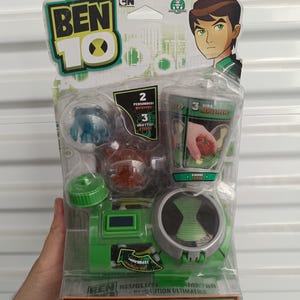 Pu&ograve; includere: Un set di giocattoli Ben 10 Revolution Ultimatrix in una confezione di plastica trasparente. La confezione presenta il logo Ben 10, illustrazioni di personaggi e il testo "Revolution Ultimatrix". Il giocattolo &egrave; principalmente verde e grigio.