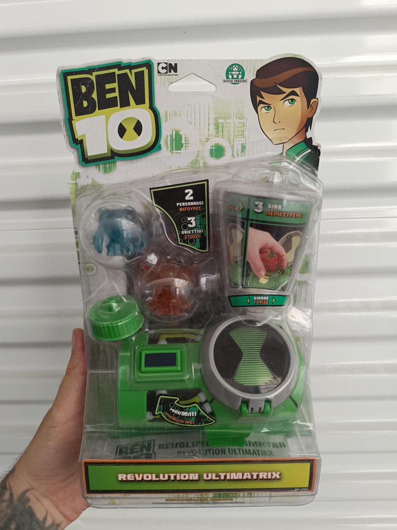 Pu&ograve; includere: Un set di giocattoli Ben 10 Revolution Ultimatrix in una confezione di plastica trasparente. La confezione presenta il logo Ben 10, illustrazioni di personaggi e il testo "Revolution Ultimatrix". Il giocattolo &egrave; principalmente verde e grigio.