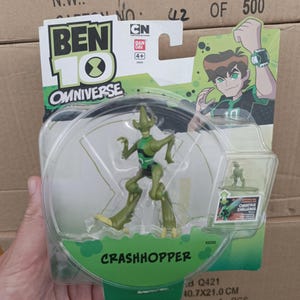 Puede incluir: Una figura de acci&oacute;n de Crashhopper de Ben 10 Omniverse en un paquete de pl&aacute;stico transparente. La figura es verde y negra, con el nombre "Crashhopper" impreso en el embalaje. El embalaje tambi&eacute;n presenta una imagen de dibujos animados de Ben 10.