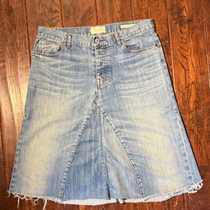 Può includere: Gonna di jeans blu chiaro con orlo sfilacciato. La gonna ha un classico design a cinque tasche, una chiusura con bottoni e una cerniera. Il denim ha un lavaggio sbiadito.