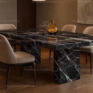 Puede incluir: Una mesa de comedor de mármol negro con vetas blancas, sostenida por dos pedestales rectangulares. La mesa está rodeada de seis sillas tapizadas beige con patas de madera oscura. Un jarrón y una escultura decorativos de cristal están sobre la mesa.