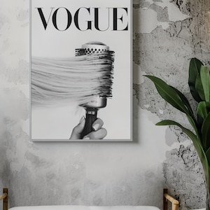 May include: Black and white framed print featuring the word "VOGUE" in bold letters. The image shows a round hairbrush with long, flowing hair. The print is displayed on a textured gray wall, with a bench and plant in the foreground.