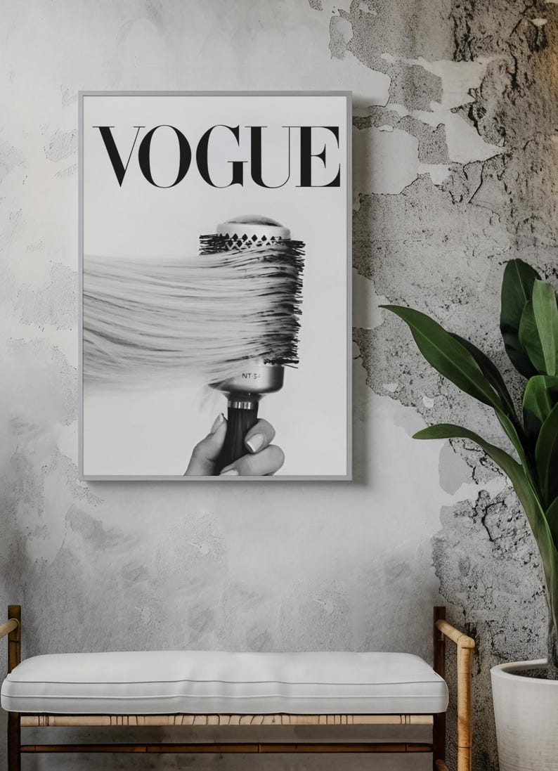 May include: Black and white framed print featuring the word "VOGUE" in bold letters. The image shows a round hairbrush with long, flowing hair. The print is displayed on a textured gray wall, with a bench and plant in the foreground.