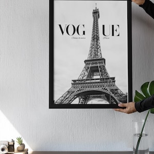 May include: Monochrome framed print of the Eiffel Tower. The print displays the word "VOGUE" at the top, with "Champ de mars" and "Paris" below. The image is held up by a person.