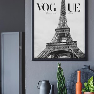 May include: Monochrome framed print of the Eiffel Tower with the word "VOGUE" at the top. The text "Champ de mars" and "Paris" are below "VOGUE". Decorative items, including vases and plants, are displayed on a grey surface.