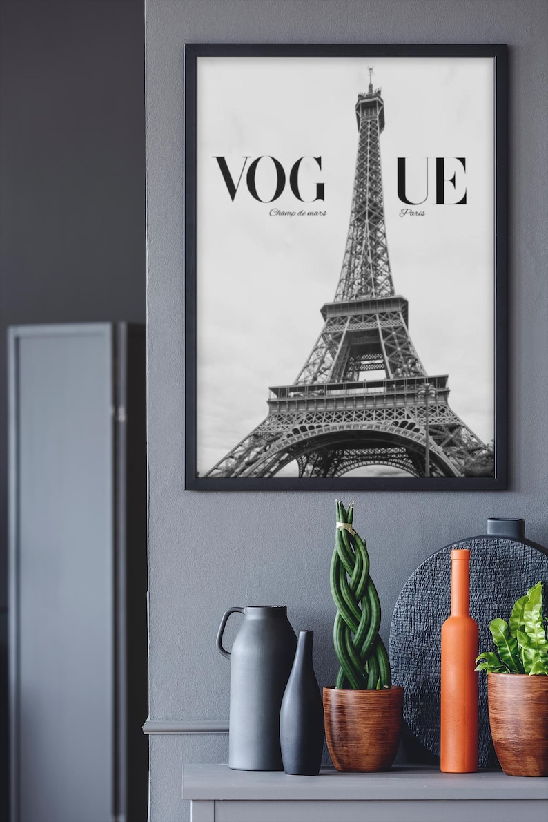 May include: Monochrome framed print of the Eiffel Tower with the word "VOGUE" at the top. The text "Champ de mars" and "Paris" are below "VOGUE". Decorative items, including vases and plants, are displayed on a grey surface.