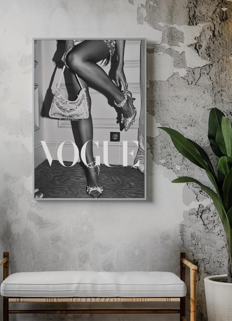 May include: Black and white framed Vogue print. The image features a person wearing high heels and holding a handbag. The word "VOGUE" is prominently displayed in large letters. The print is displayed on a textured gray wall.
