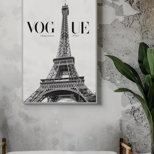 May include: Monochrome framed print of the Eiffel Tower in Paris. The word "VOGUE" is at the top, with "Champ de mars" and "Paris" below. The print is displayed on a grey wall above a white bench.