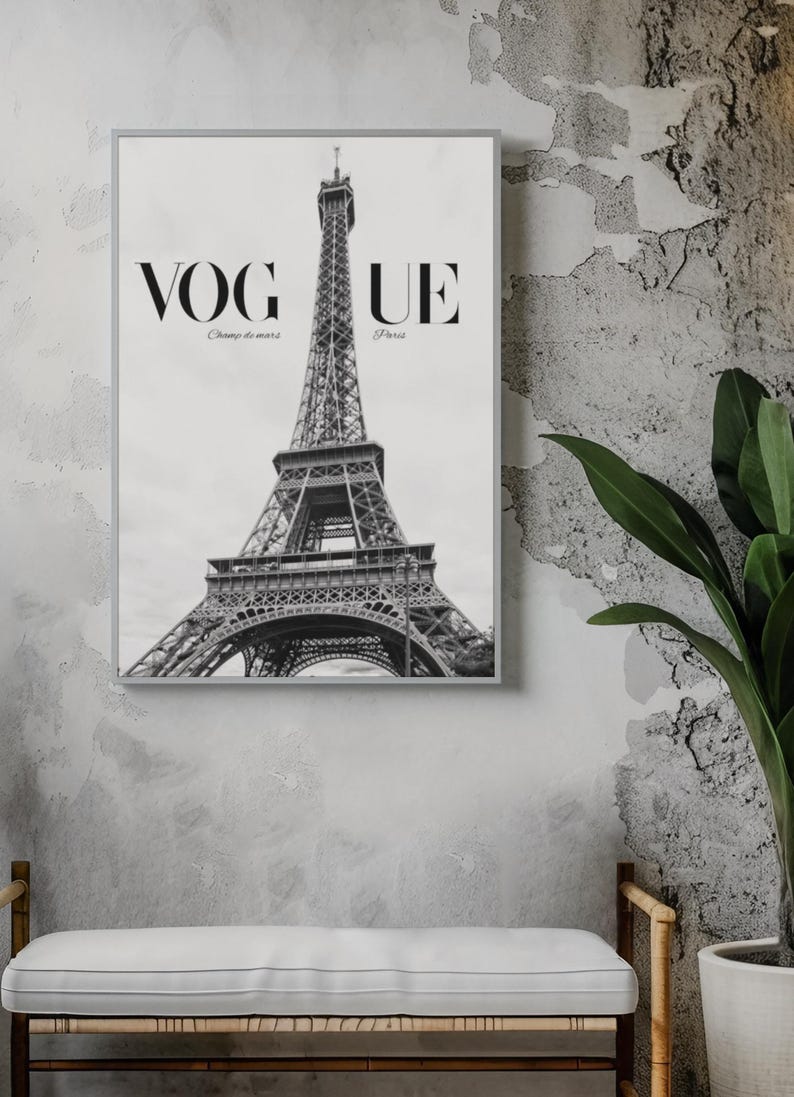 May include: Monochrome framed print of the Eiffel Tower in Paris. The word "VOGUE" is at the top, with "Champ de mars" and "Paris" below. The print is displayed on a grey wall above a white bench.