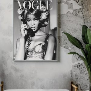Może przedstawiać: Czarno-białe zdjęcie oprawionej okładki magazynu Vogue. Przedstawia kobietę z wałkami do włos&oacute;w trzymającą słuchawkę telefonu. Logo Vogue jest na g&oacute;rze. Obraz wisi na teksturowanej szarej ścianie.