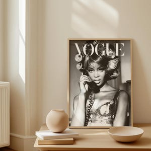 Może przedstawiać: Czarno-biała oprawiona okładka magazynu Vogue z kobietą w wałkach i telefonem. Obraz znajduje się na drewnianym stole z wazonem, książkami i miską. Styl vintage i stylowy.