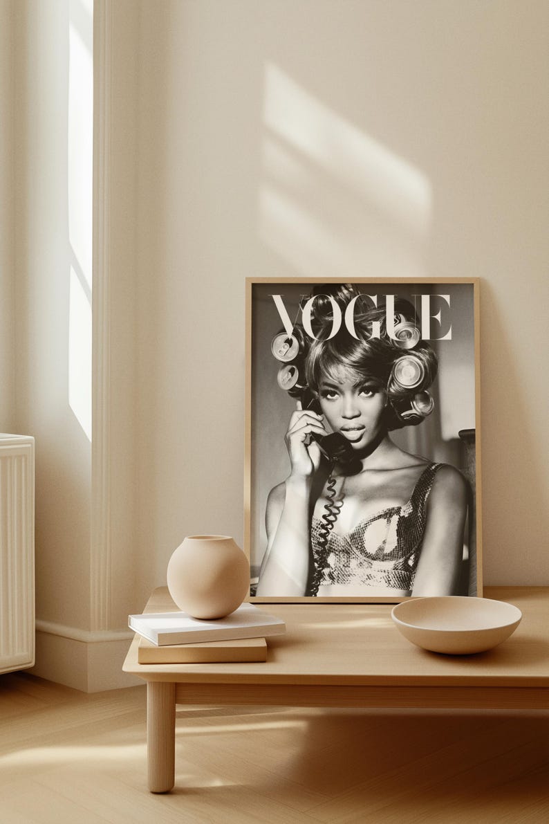 Może przedstawiać: Czarno-biała oprawiona okładka magazynu Vogue z kobietą w wałkach i telefonem. Obraz znajduje się na drewnianym stole z wazonem, książkami i miską. Styl vintage i stylowy.