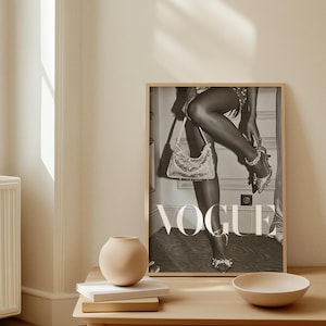 May include: A framed black and white Vogue magazine cover print. The image features a person wearing embellished high heels and holding a sequined handbag. The word "VOGUE" is prominently displayed in large white letters.