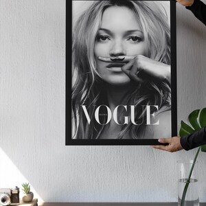 May include: Black and white framed Vogue magazine cover featuring a woman with a finger moustache. The word "VOGUE" is displayed. The image is held up by a person.