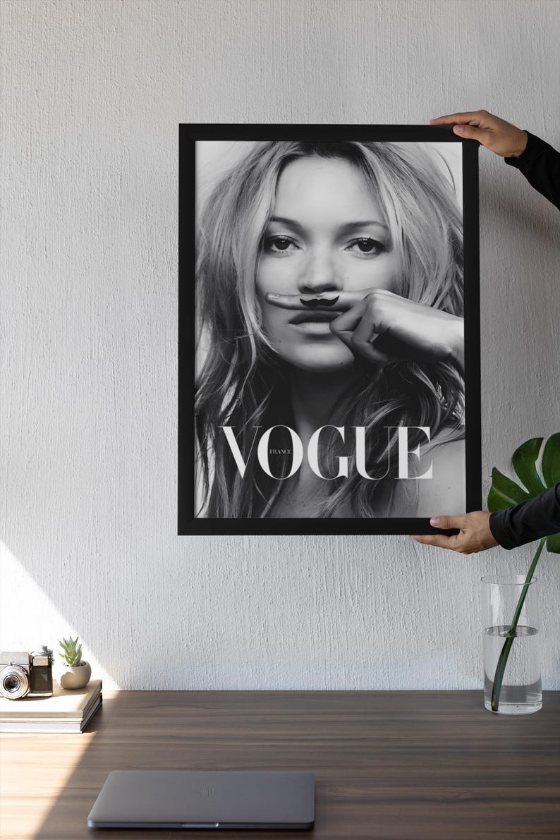 May include: Black and white framed Vogue magazine cover featuring a woman with a finger moustache. The word "VOGUE" is displayed. The image is held up by a person.