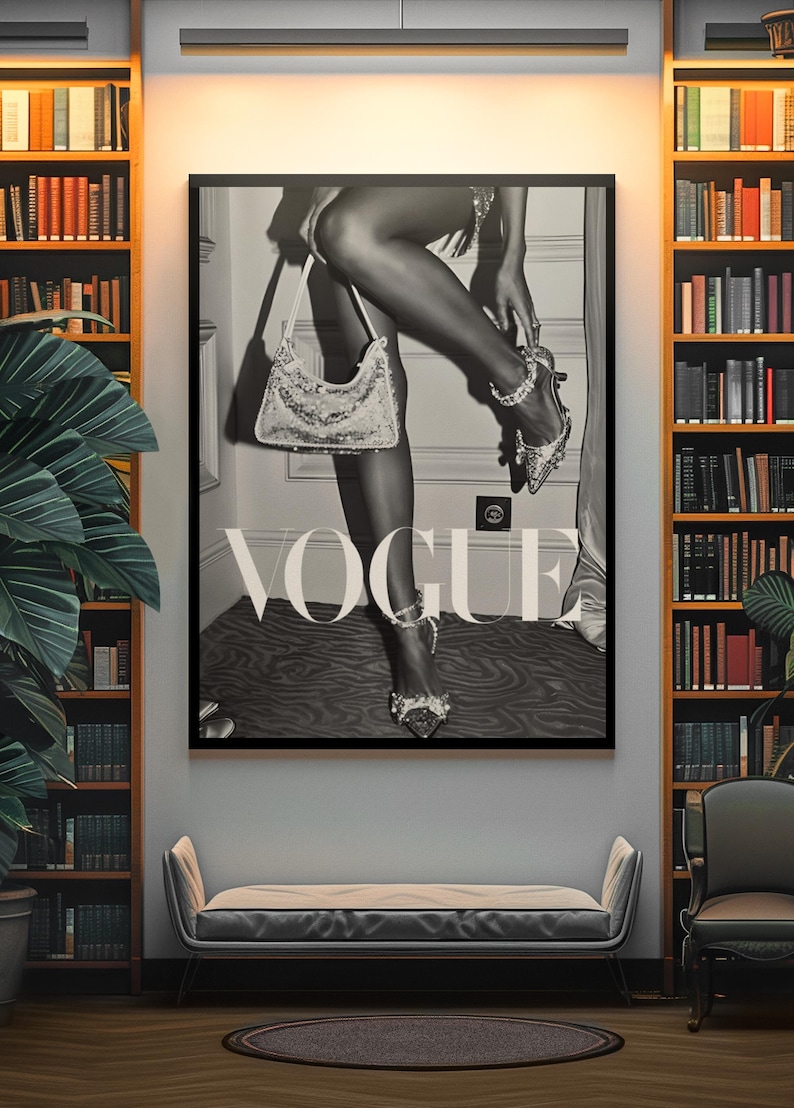 May include: Black and white Vogue poster featuring a woman adjusting a jeweled shoe, holding a sequined purse. The poster is framed and displayed in a room with bookshelves, a bench, and a chair.