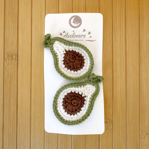 May include: Two crocheted avocado-shaped appliques on a white display card labeled Aselovers Personalized Baby Gifts. Each piece features a dark green outer border, a white inner section, and a textured brown center representing the avocado pit.