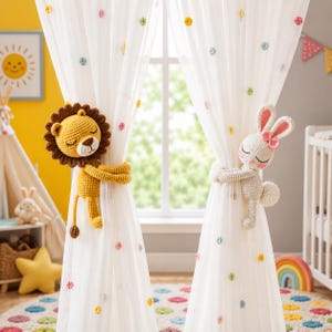 May include: Two sheer white curtains featuring small colourful embroidered dots, held back by a crocheted yellow lion and a crocheted white rabbit. The lion has a brown mane and closed eyes, while the rabbit has pink inner ears and closed eyes.