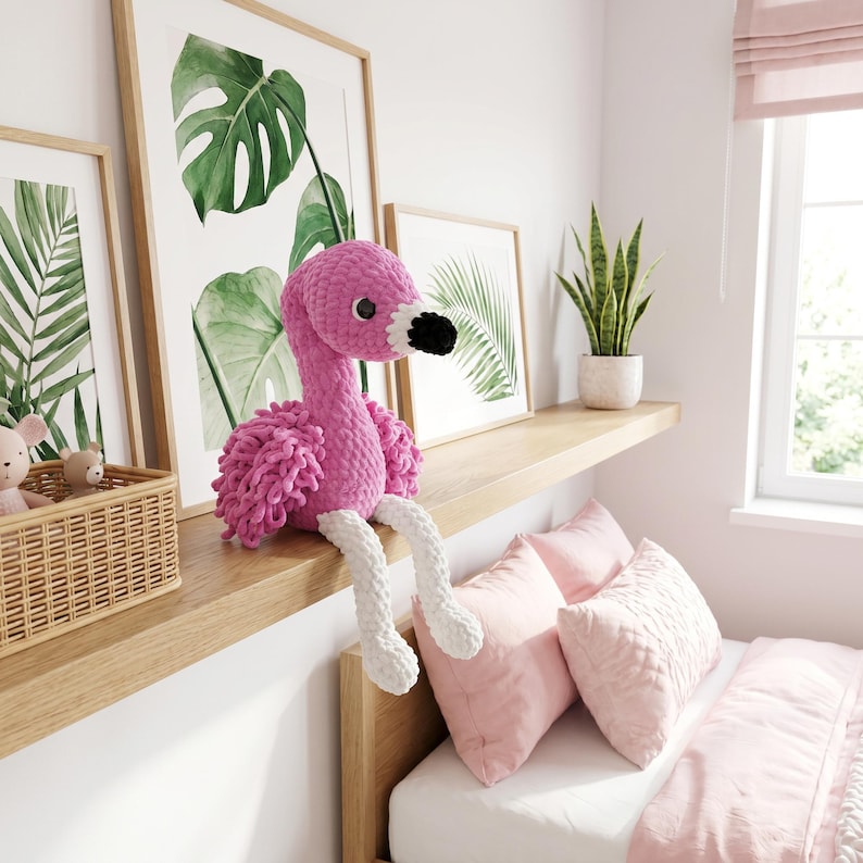 Pink crochet flamingo plush toy sitting on nursery window shelf, handmade amigurumi bird decor for baby girl bedroom, soft stuffed animal gift