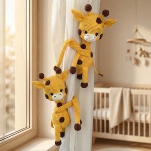 May include: Two yellow crochet giraffe curtain tiebacks featuring dark brown spots, small horns, and white muzzles. Each giraffe has long, flexible arms designed to wrap around and secure a white fabric curtain panel in a nursery setting.