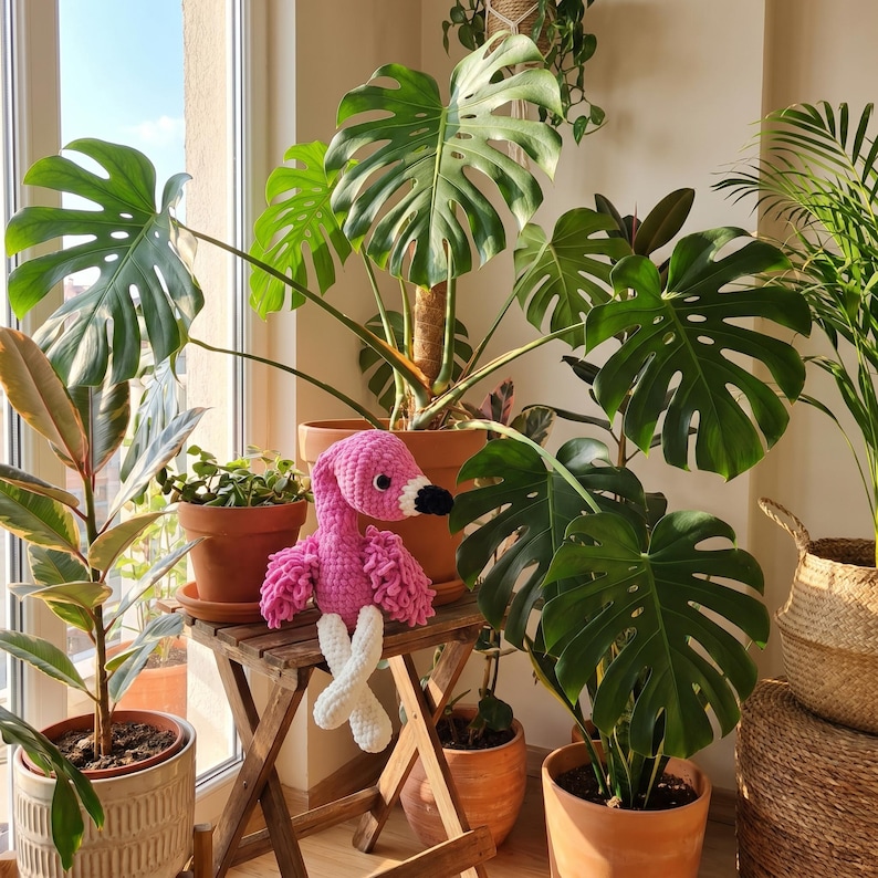 Pink crochet flamingo plush surrounded by tropical plants, unique nursery decoration