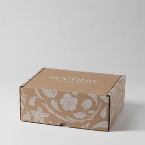 Puede incluir: Una caja de cartón marrón con un estampado floral blanco y el texto "scentsy WHIFF BOX". La caja está cerrada y tiene forma rectangular. El diseño floral incluye flores y hojas.