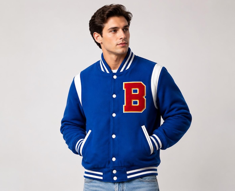 May include: A royal blue varsity jacket with white accents on the shoulders, collar, and cuffs. The jacket features a large red letter "B" on the chest, a button-up front, and two front pockets. The jacket is a classic style.