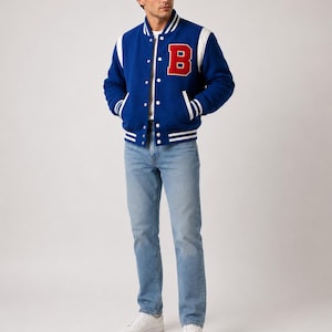 May include: A blue varsity jacket with white accents and a large red "B" on the chest. The jacket has a button-up front and white stripes on the cuffs and hem. The person is wearing light blue jeans and white sneakers.