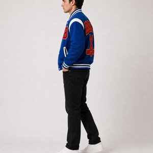May include: A blue varsity jacket with white and red accents. The jacket features the word "Bruins" and crossed hockey sticks on the back. The jacket has a button-up front, white stripes on the cuffs and hem, and a white collar.